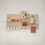 Standard pegboard -  wall organizer mounted on a white wall, styled with a white vase of dried flowers, a small basket, a paper towel holder, glass cups, white teacups hanging below, and a cork note holder.