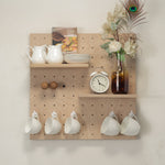 Small pegboard - styled with white ceramic pitchers, stacked plates, a vintage-style alarm clock, a glass bottle with dried flowers and a peacock feather, and four white mugs hanging from the bottom pegs.