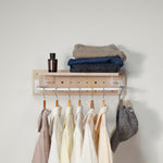 Tiny pegboard - with a white hanging rod, shown holding folded clothes, a small bottle, and a cap against a plain off-white wall.